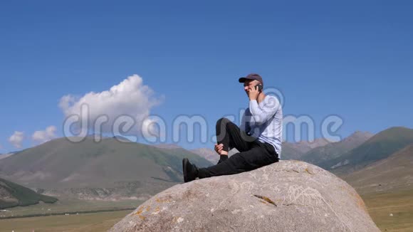 坐在大石头上的人用手机打电话视频的预览图