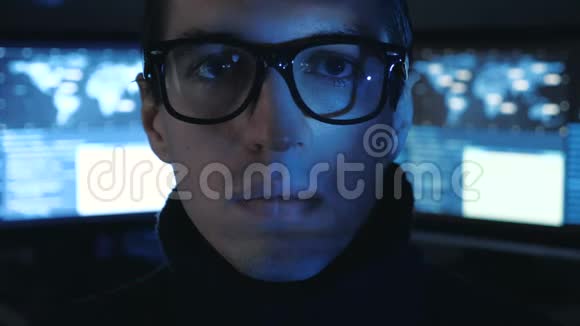 戴眼镜的Hacker程序员的肖像看着相机而蓝码字符在网络中反射他的脸视频的预览图