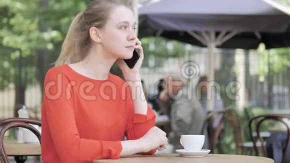 年轻女子打电话坐在咖啡厅露台视频的预览图