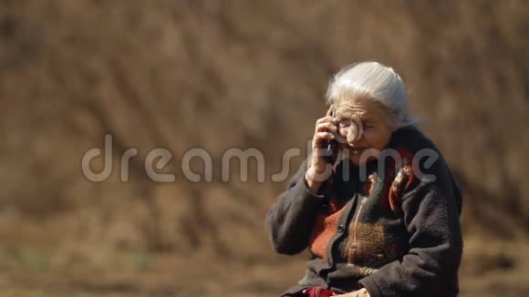 一位老妇人坐在公园里用手机说话的慢镜头肖像视频的预览图