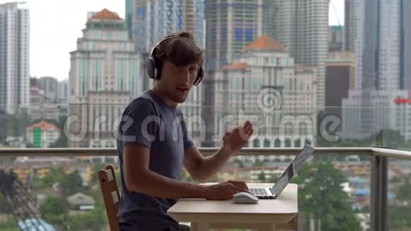 年轻的自由职业者在阳台上的笔记本电脑上工作背景是一个充满摩天大楼的市中心自由职业者视频的预览图