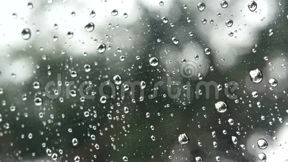 4K镜头雨水在透明的窗户玻璃表面绿色的树和外面的背景雨滴视频的预览图