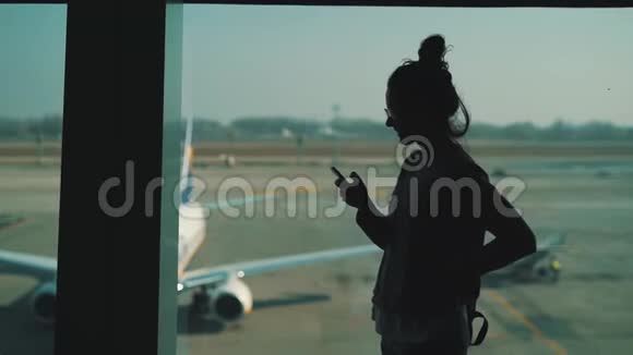 女孩在机场候机楼的窗口使用智能手机视频的预览图