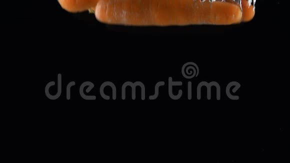 整根胡萝卜掉在黑色背景上的水里视频的预览图