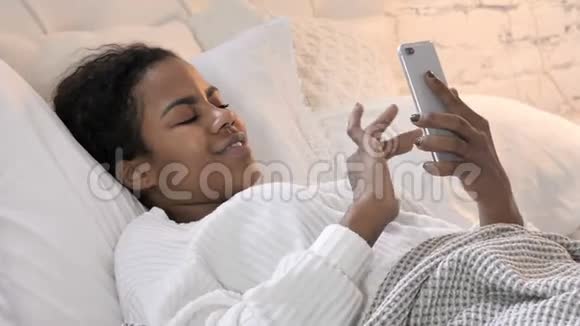 年轻的非洲妇女在床上使用智能手机视频的预览图