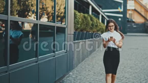 年轻漂亮聪明的商务女孩穿着商务服走路在这段时间里她把手机拿在手里视频的预览图