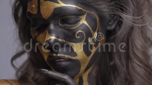 美丽的女人她的脸颊上有一只蝴蝶摆着黑色和金色的身体艺术视频的预览图