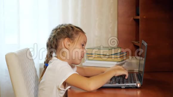 小女孩在桌子上用笔记本电脑视频的预览图