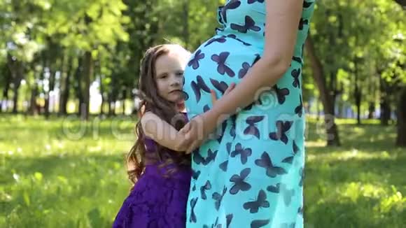 一个小女孩在草地上的公园里拥抱她怀孕的母亲视频的预览图