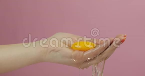 女人手上的新鲜鸡蛋手握蛋黄在粉红色背景上视频的预览图