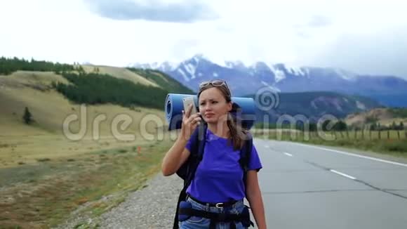 年轻的旅游妇女带着背包和太阳镜试图在山路上捕捉电话信号有很多视频的预览图