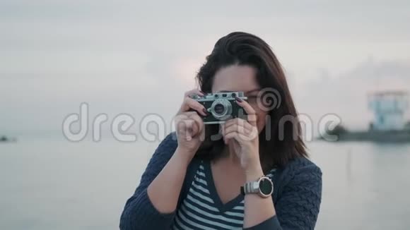 一个带复古相机的女孩的肖像年轻女子在海边的老式照相机上拍照视频的预览图
