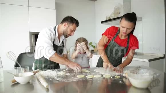 可爱的小女孩和她美丽的父母在做饭他们在一起玩得很开心在家里的厨房里微笑视频的预览图