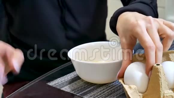 女人的手在厨房把一个鸡蛋打碎成一个白色的陶瓷碗视频的预览图