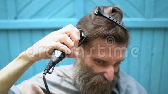 奇怪的时髦男人留着大灰头发的胡子和可笑的鬼脸试图用电动剃须刀剪头发视频的预览图