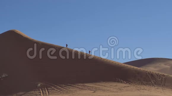 两个徒步旅行者在沙漠沙丘上爬上斜坡边缘视频的预览图