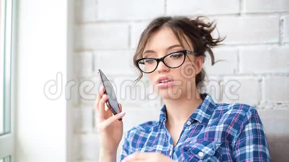 一个年轻的卷发美女戴着眼镜穿着莫特利衬衫在舒适的智能手机上说话视频的预览图