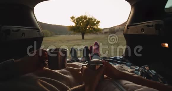 捕捉一对夫妇在汽车后备箱中的细节在大自然中舒适的袜子和拿着一杯铁茶视频的预览图
