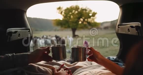 浪漫的情侣在乡下玩得很开心他们坐在汽车后备箱里穿着舒适的袜子喝茶视频的预览图