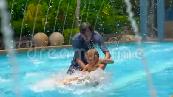 一位年轻的父亲和他的儿子在喷泉间的一个热带水池里玩得很开心视频的预览图