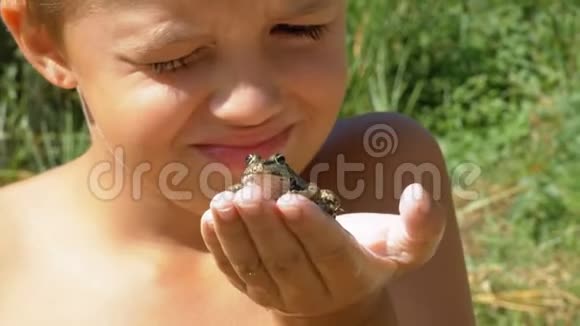 小男孩手里拿着一只青蛙在河边的海滩上用手指敲击蟾蜍视频的预览图