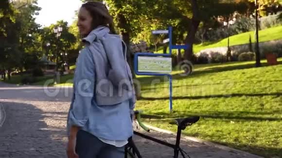 美丽的年轻的快乐的女人在早晨的公园里除了一辆自行车那个女孩骑着她的徒步自行车走路视频的预览图