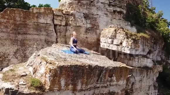 在山上做瑜伽姿势的女孩鸟瞰美丽的自然和峭壁视频的预览图