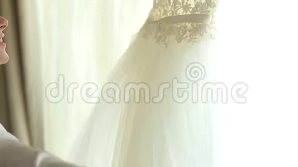 新娘穿着丝绸礼服在窗前欣赏她的婚纱视频的预览图