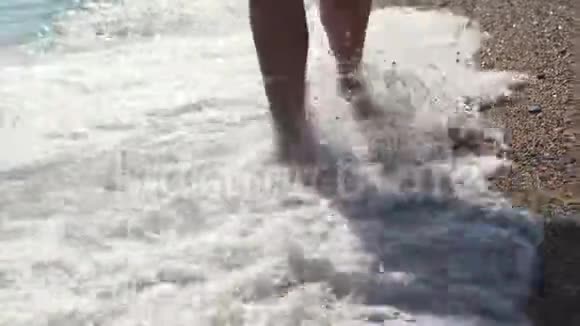 穿着凉鞋的女性双脚踩着沙滩上的沙子和鹅卵石特写镜头视频的预览图