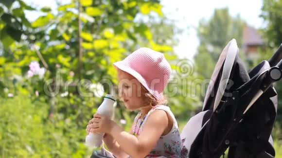 小女孩坐在婴儿车里喝着一瓶牛奶或啤酒视频的预览图