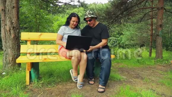 一个男人和一个女人在一个长凳上的公园里讨论他们在笔记本电脑上读到的东西视频的预览图