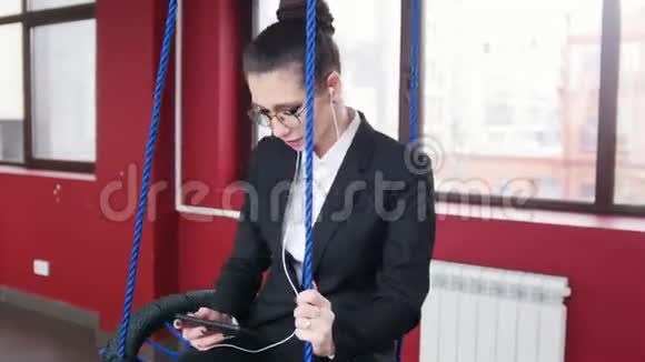 商业概念一个女人坐在办公室的秋千上听音乐看着屏幕视频的预览图