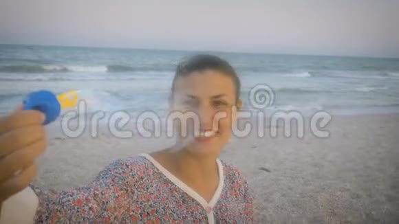 在一个多风的日子里穿着五颜六色西装的女孩在海滩上吹着肥皂泡在大海的背景下笑着视频的预览图