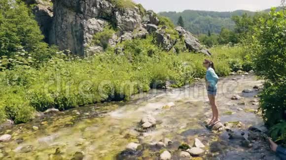 年轻女子站在河边的石头上欣赏大自然的风景视频的预览图