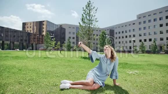 绿草上的年轻女人带着智能手机拍照自拍视频的预览图