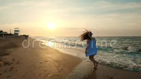 日落时女孩在浅水中奔跑一个穿着白色裙子的女孩正在水的边缘附近奔跑视频的预览图