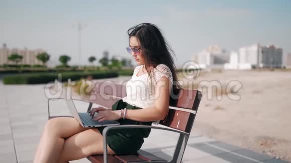 坐在户外长凳上在笔记本电脑上打字的漂亮欧洲女人的简介视频的预览图
