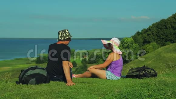 男女游客正坐在山的边缘俯瞰湖面女人打开笔记本电脑视频的预览图