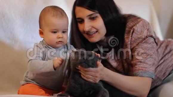 一位年轻的母亲和她的孩子坐在沙发上抚摸着猫的慢动作镜头视频的预览图