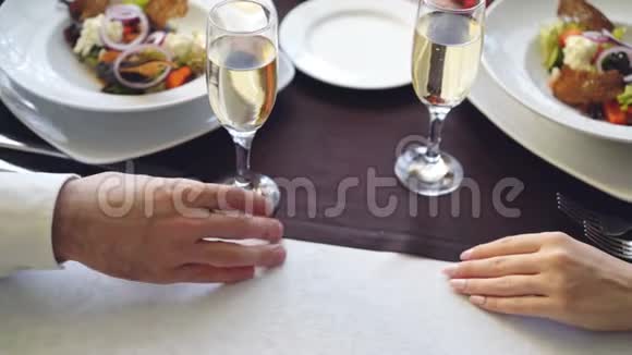 在优雅的餐厅里年轻情侣触摸和牵手的特写镜头提供起泡香槟杯的桌子视频的预览图