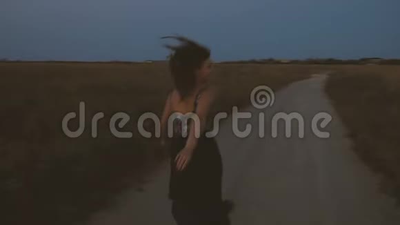 日落时分穿着一件挥舞着的裙子的女孩在夏日田野的路上跳跃旋转和欢笑视频的预览图