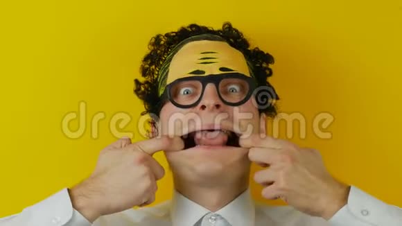 疯疯癫癫的卷发男在黄墙背景上露出舌头疯狂的情绪视频的预览图