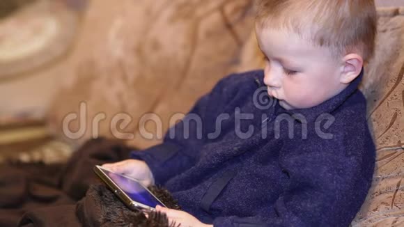 孩子在沙发上玩手机在房间里Chirld双手在智能手机上发短信他拿着一部现代手机视频的预览图