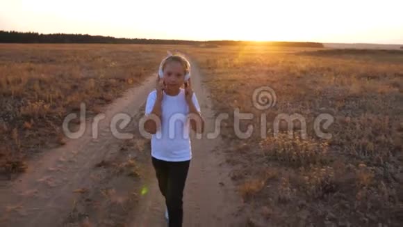 年轻女孩带着耳机在路上听音乐在夕阳下跳舞视频的预览图