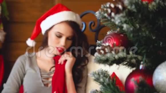 圣诞老人戴着圣诞老人帽子的年轻女子在装饰圣诞树附近的肖像很漂亮的女人微笑新年视频的预览图