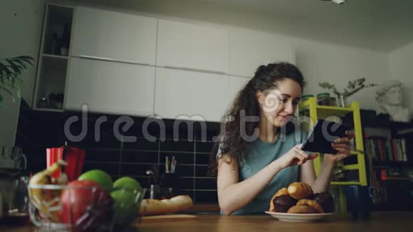 年轻漂亮的白种人女人坐在厨房的桌子上用数字平板电脑她正朝窗户看一眼视频的预览图