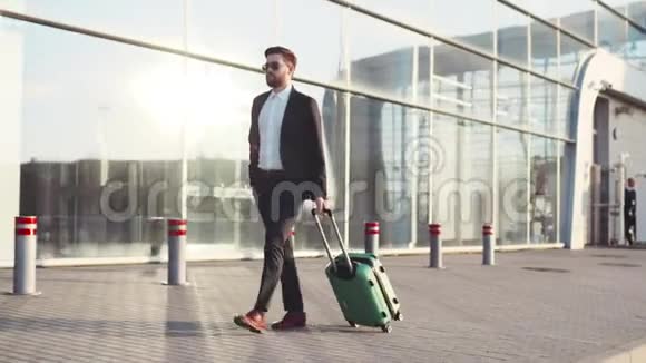 时尚的小胡子戴着太阳镜带着行李离开机场航站楼接电话商业风格视频的预览图