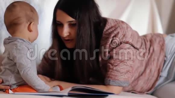 年轻的母亲是一个关心她的母亲给她的小儿子读一本书看着他他们一起微笑慢镜头视频的预览图