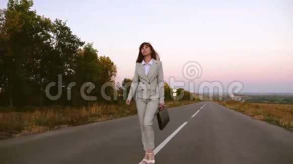 瘦削的商人女人手里拿着黑色公文包走在沥青上穿着浅色西装和白色鞋子的女孩视频的预览图
