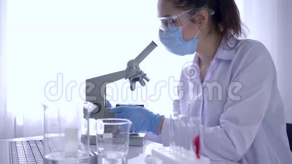现代医学研究员女孩用显微镜工作在实验室特写镜头中用笔记本电脑写数据视频的预览图